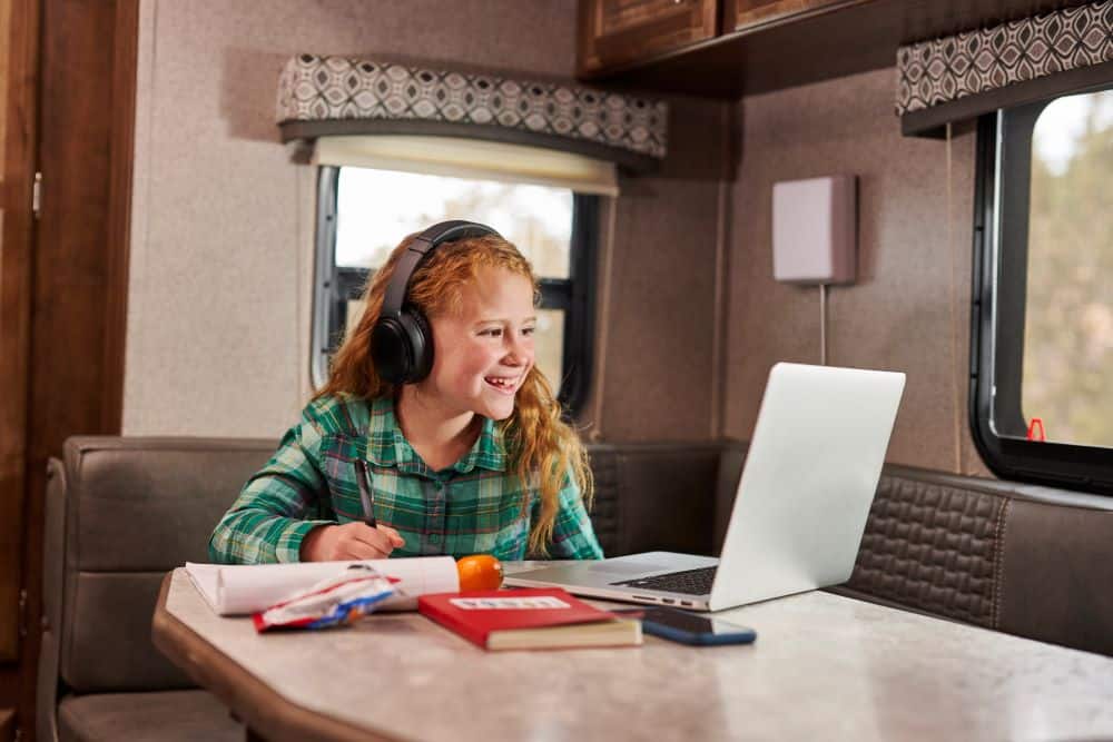 young girl sits in RV with a laptop and headphones learning remote - weBoost Destination RV