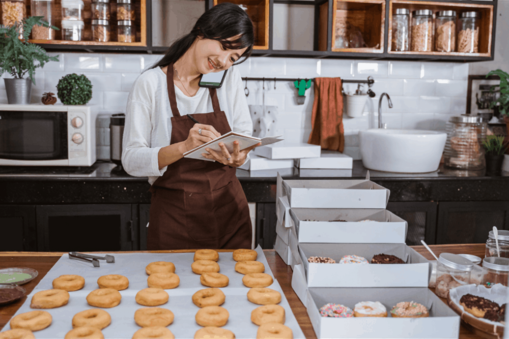 a baker talks on her cellphone while taking notes and making doughnuts