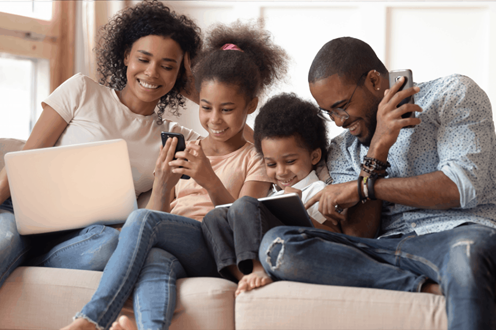 a family uses tech devices while sitting on their couch